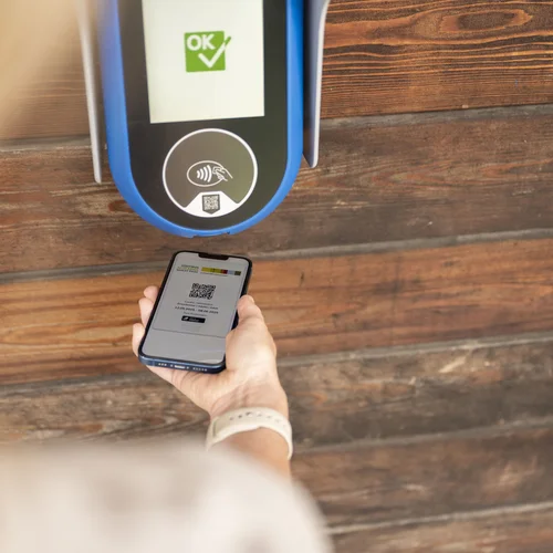 Persona scansiona un codice QR con lo smartphone su un lettore montato su una parete di legno.