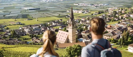 Two hikers look at a village with a church and mountains in the background.
