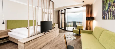 Modern hotel room with green sofa, bed and balcony with mountain view