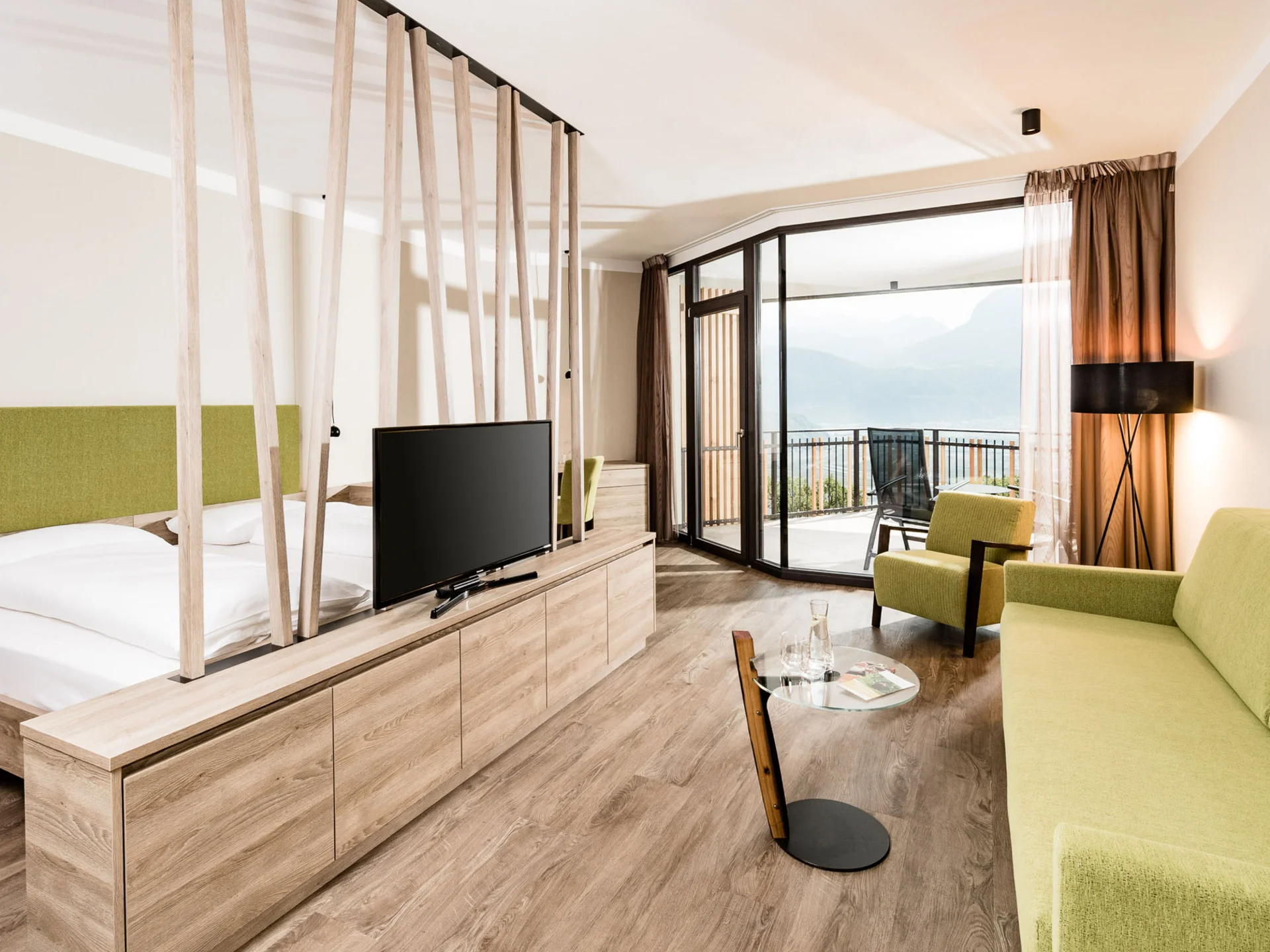 Modernes Hotelzimmer mit grünem Sofa, Bett und Balkon mit Bergblick
