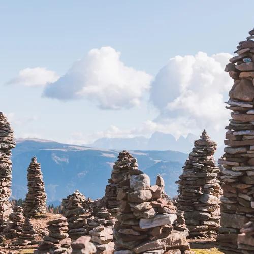 Places of interest in Tramin and the surrounding area Several tall piles of stones in front of a mountain landscape and a blue sky with clouds.