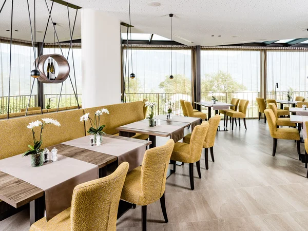 Ristorante luminoso con sedie gialle e tavoli decorati con fiori su runner.