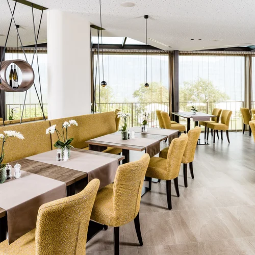 Ristorante luminoso con sedie gialle e tavoli decorati con fiori su runner.