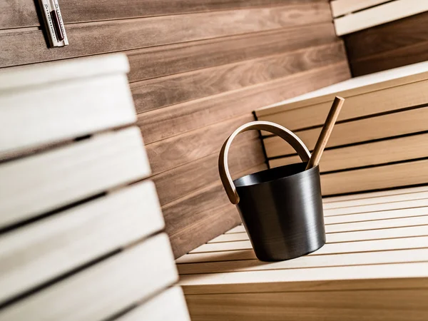 Secchio da sauna nero con mestolo in legno su panche di legno in una sauna