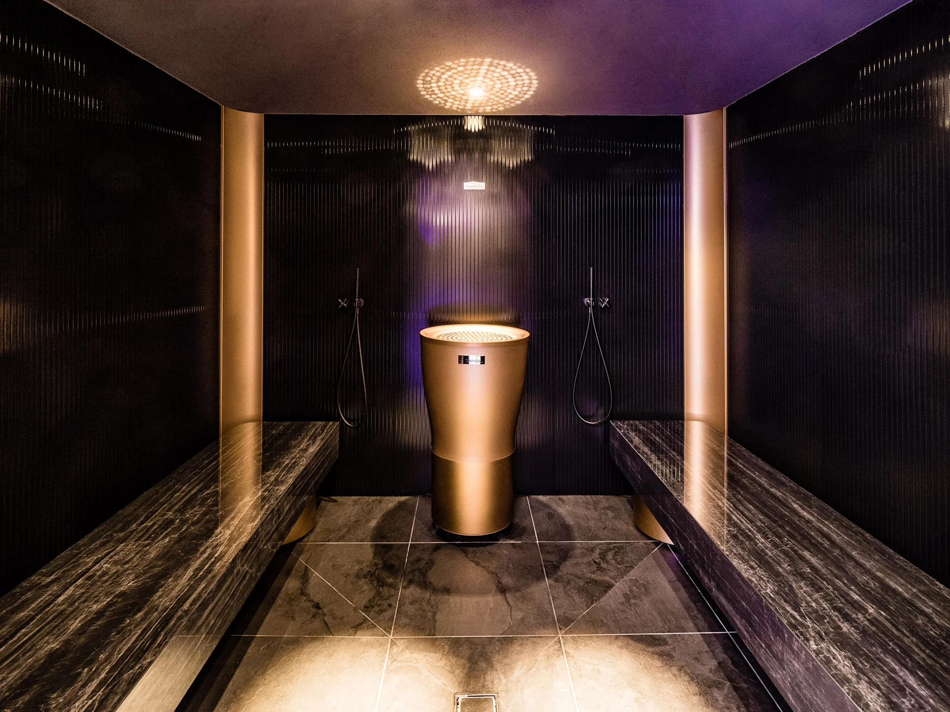 Modern steam bath room with gold-colored steam generator and marble benches.