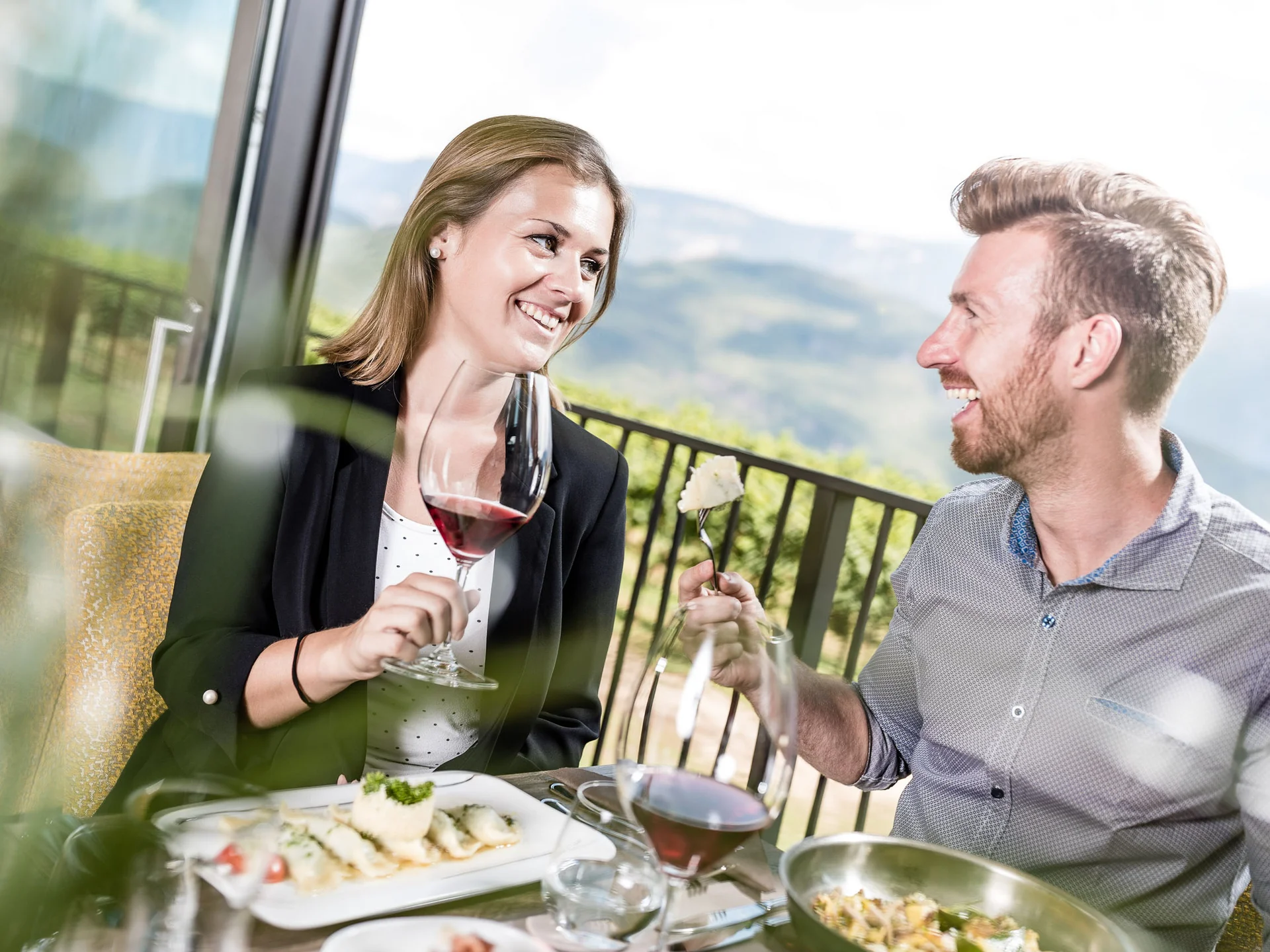 Paar genießt Wein und Essen auf Terrasse mit Bergblick