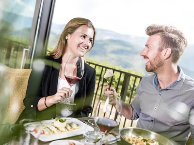 Paar genießt Wein und Essen auf Terrasse mit Bergblick