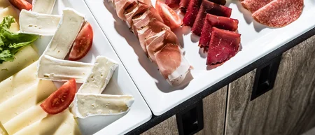 Various types of cheese and cold cuts on white plates with tomatoes and salad.