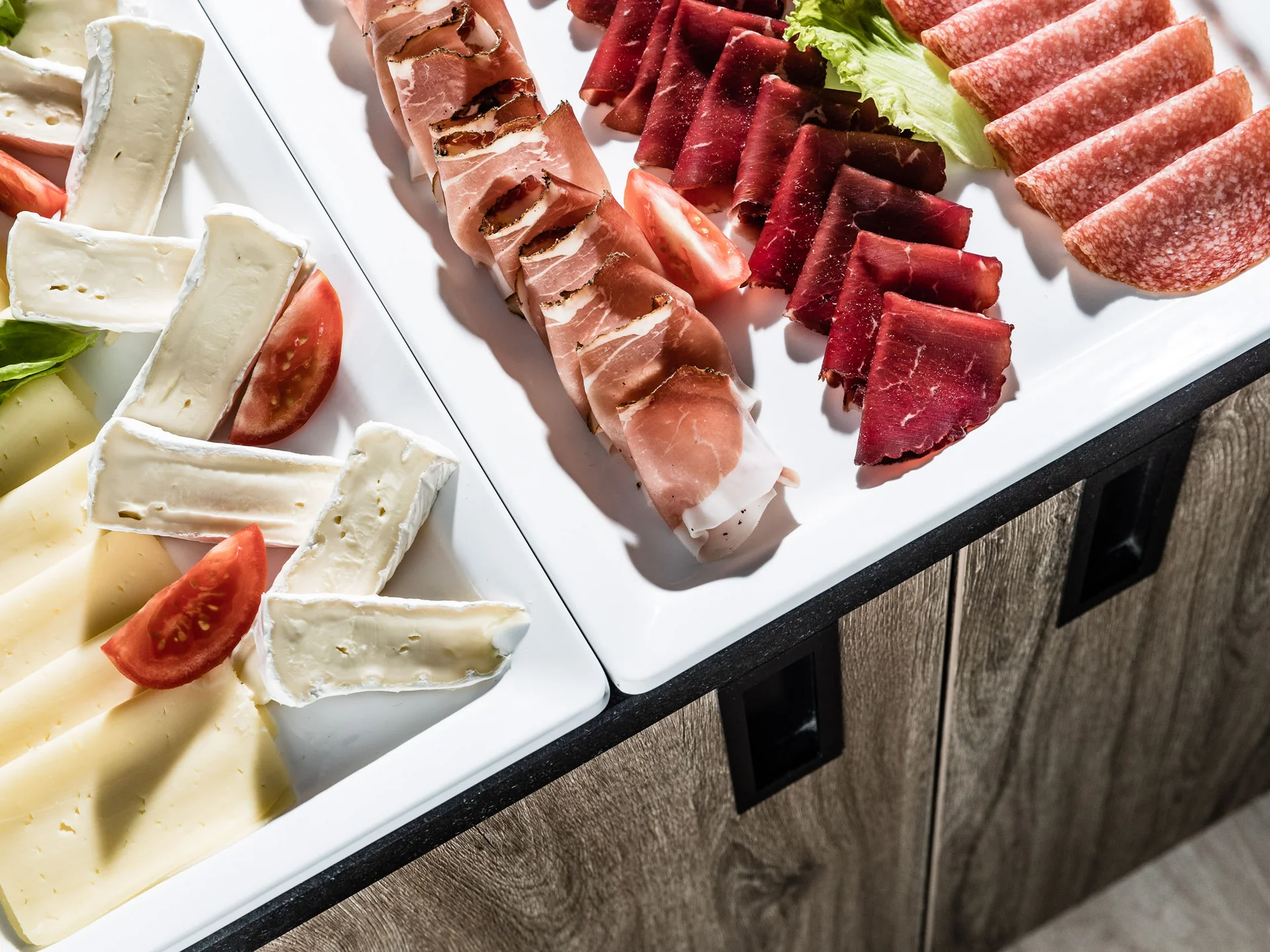 Verschiedene Käsesorten und Aufschnitt auf weißen Tellern mit Tomaten und Salat