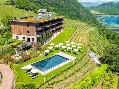 Il vostro hotel a Termeno: un angolo di pace tra i vigneti Hotel con piscina e ombrelloni tra i vigneti in un paesaggio collinare