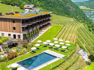 Hotel mit Pool und Sonnenschirmen zwischen Weinbergen in hügeliger Landschaft