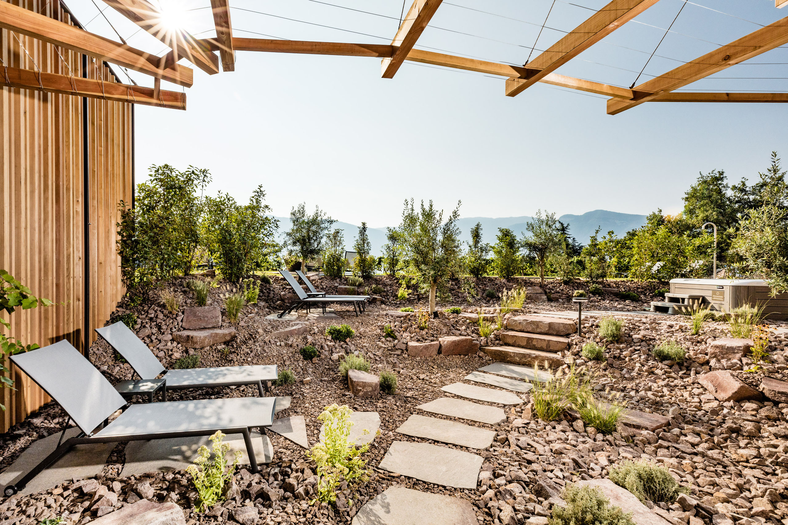 Bildergalerie: Eindrücke aus dem Plattenhof in Tramin Garten mit Liegestühlen, Steintreppe und Holzpergola bei sonnigem Wetter